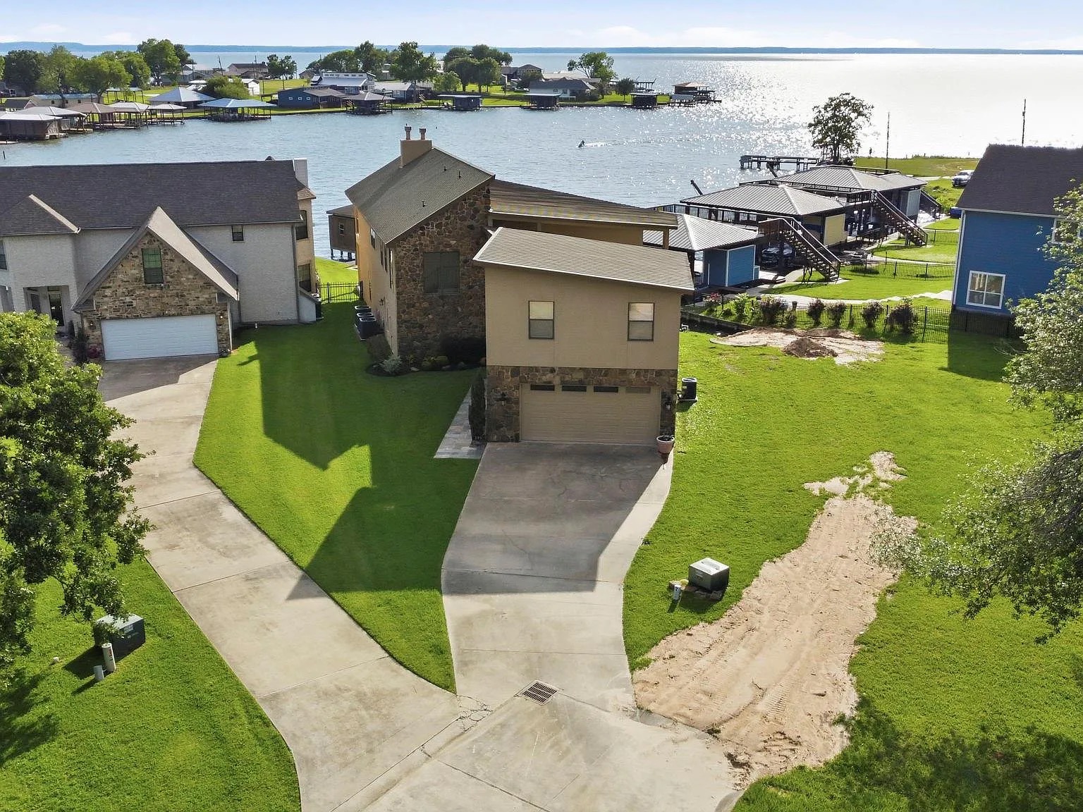 Aerial view of 295 Bayview Lane from above the canal, the stone residence centered on its lot with Lake Livingston stretching to the horizon and neighboring docks on either side